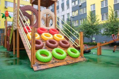 Yağmurlu bir yaz gününde ağaçtan ve plastikten yapılmış modern ve büyük bir oyun alanı olan yüksek binalardan oluşan bir avlu. Açık hava çocuk parkı. Çocuk oyunları ve spor için bir yer.