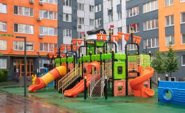 Yağmurlu bir yaz gününde yağmurlu bir günde modern renkli ve büyük bir oyun parkı olan yüksek binalardan oluşan bir avlu. Açık hava çocuk parkı. Çocuk oyunları ve spor için bir yer.