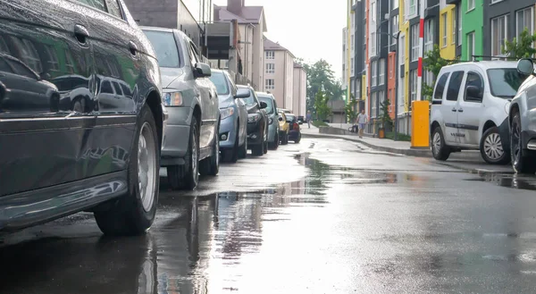 Street in a city without people with parked cars in rainy weather. Rain on the road. Rain and cars. Background of parked cars on a rainy city street. Symmetrical parked cars