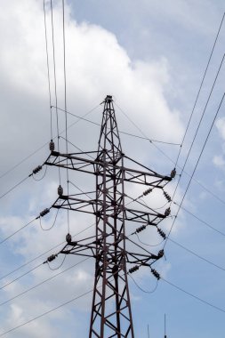 Yüksek voltajlı elektrik kulesi. Güneşli bir günde mavi gökyüzünde dairesel bulutlar olan elektrik hatları ve elektrik direkleri. Yüksek voltajlı güç iletim hattı destekliyor. Karmaşık bir çelik yapıları var.