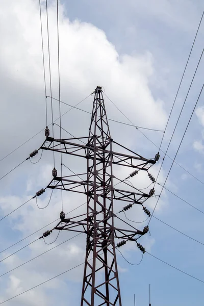 Yüksek voltajlı elektrik kulesi. Güneşli bir günde mavi gökyüzünde dairesel bulutlar olan elektrik hatları ve elektrik direkleri. Yüksek voltajlı güç iletim hattı destekliyor. Karmaşık bir çelik yapıları var.