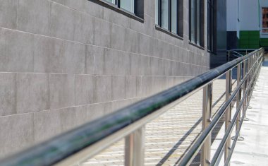 Tekerlekli sandalyeler, bisikletler ve binanın önünde çocuklu pusetler için paslanmaz çelik tırabzanlar olan bir rampa. Tekerlekli sandalye kaldırmak için tırabzan. Parlak paslanmaz çelik korkuluklar
