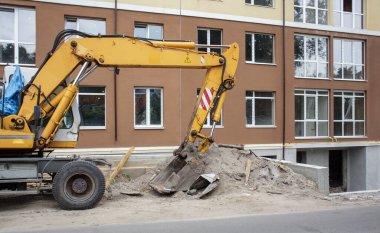 İnşaat halindeki bir binanın arka planında sarı renkli mobil vinç yükleyicisi var. Alman-İsviçreli uluslararası ekipman üreticisi. Kazı makinesi toprak işlerinde kullanılır.
