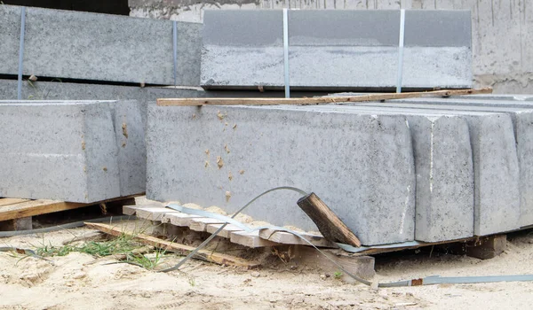 Faceted granite curbs on a pallet. Smooth porcelain stoneware products at the construction site. Curbstone, a stack of concrete curb boards prepared for installation. Road repair