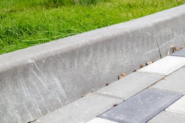 Beton kaldırımların kurulumu. Yol altyapısı tamiri. Yeşil çimenler beton kaldırım tarafından ayrılmış asfalt levhaların yanında yetişir. Yol ve çimenler ayrılmış.