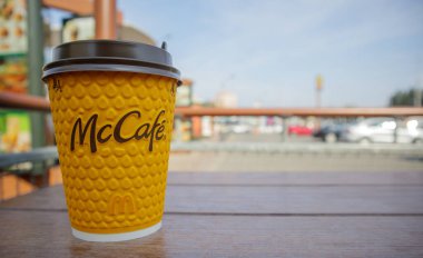 McDonald 's' ın bulanık şehrine karşı masada McCafe için kahve ve kağıt sarısı cam bardak. Fast food işi geçmişi. Fast food restoran menüsü. Ukrayna, Kiev - 13 Eylül 2021