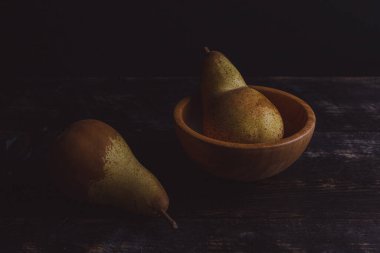 Taze olgun organik armutların yakın plan görüntüsü ve karanlık yüzeyde kâse.