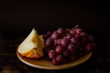 Mor üzüm ve kavun diliminin koyu arkaplanda fotoğrafı.