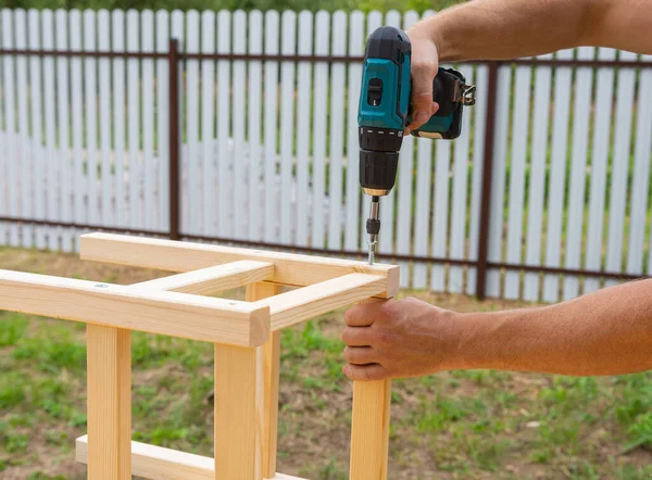 action, assembling a wooden stool with an electric screwdriver, the photo was taken outside on a cloudy day,