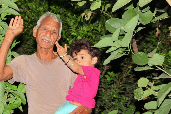 A beautiful Indian child and grandfather smile at the garden looking at the growing beauty of the trees, india