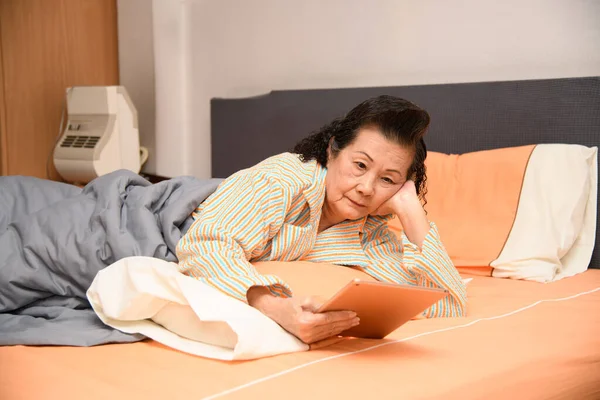 Büyükannem yatak odasındaki yatakta tabletle oynuyor..