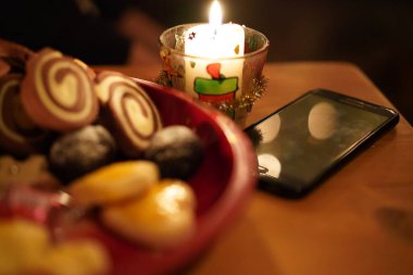 Siyah cep telefonu ahşap bir masada, kırmızı bir tabakta mum ışığı ve hamur işi ile çevrimdışı duruyor. Kavramların bulanık arkaplanı.