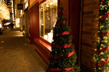 Karanlık akşamlarda çam ağacı, kırmızı kurdele, ışık ve çelenk ile süslenmiş ve aydınlatılmış bir mağaza penceresi. Rennweg 'de Noel alışverişi, Bahnhofstrasse Zürih' in bir yan sokağı. Zürih, 19 yaşında. Aralık 2020.