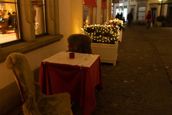 Empty chair and table of a restaurant in old town of Zurich in Christmas time during corona pandemic time. Pedestrian in blurred background. Zurich, 19. December 2020.