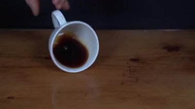 Siyah arka planlı ahşap masanın üzerine bir fincan kahve dökerek..