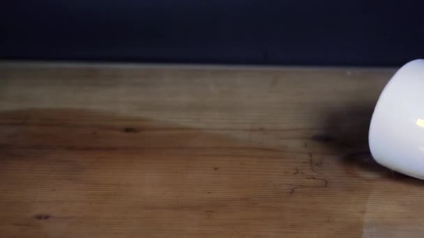 Šplouchající šálek kávy na dřevěném stole s černým pozadím.