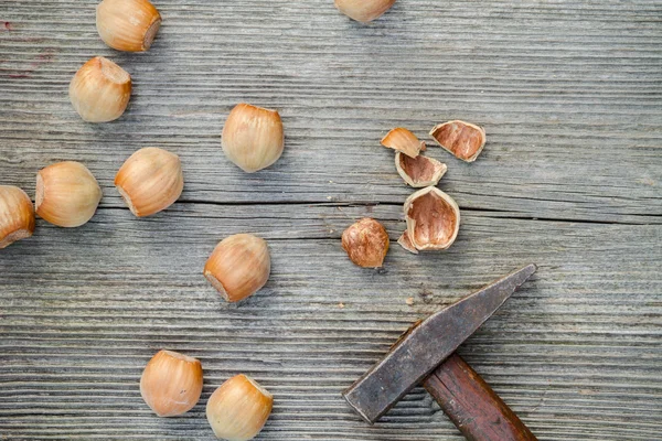 Cracked nuts and hammer on old wooden background — Stock fotografie