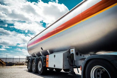 Karavanlı bir kamyon, yanıcı sıvılı bir tank, güneşli bir gün dışarıda, metalik renk kabı, beyaz bulutlu mavi gökyüzü, çakıl