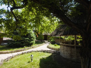 Bungalov, gölgede yeşil bir çimenlikte güneşli bir yaz gününde, ağaçların ve çam ağacının yanında ahşap yollar ve gece fenerleri.