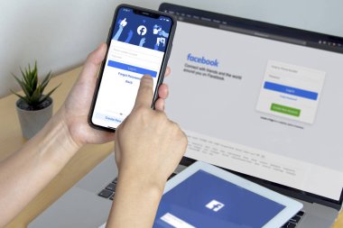 Calgary, Alberta. Kanada mı? 11 Kasım 2020: iPhone Pro 12, iPad ve tahta bir masada Macbook Pro 'da Facebook uygulaması kullanan bir kişi.