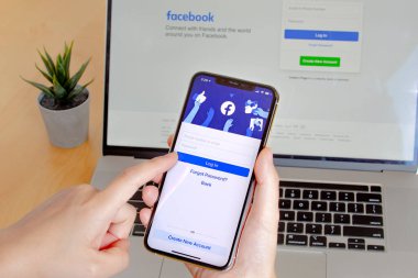 Calgary, Alberta. Kanada mı? 11 Kasım 2020: Facebook uygulamasını iPhone Pro 12 ve Macbook Pro 'yu bir bitkiyle birlikte ahşap bir masada kullanan bir kişinin yakın çekimi.