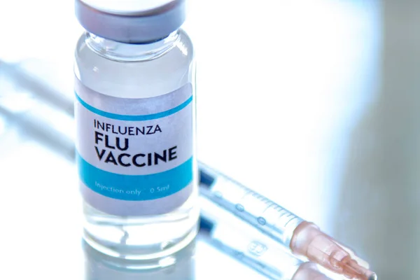 A Bottle of Influenza Flu vaccine on a Sterile Transparent Vial with a injection Syringe on a reflective surface. Concept: Influenza Flu Vaccine vaccine