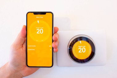 Kalorifer açıkken iPhone 11 Pro Max 'i akıllı bir termostatın yanında tutan kişi..