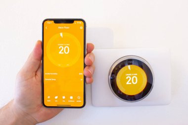 Calgary, Alberta, Kanada. Ocak 03 2021. Kalorifer açıkken iPhone 11 Pro Max 'i akıllı bir termostatın yanında tutan kişi..