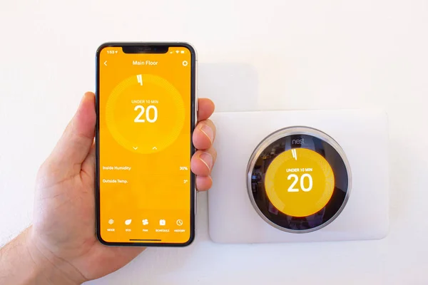 stock image Calgary, Alberta, Canada. Jan 03 2021. A person holding an iPhone 11 Pro Max next to a Nest smart thermostat while the heat is on.