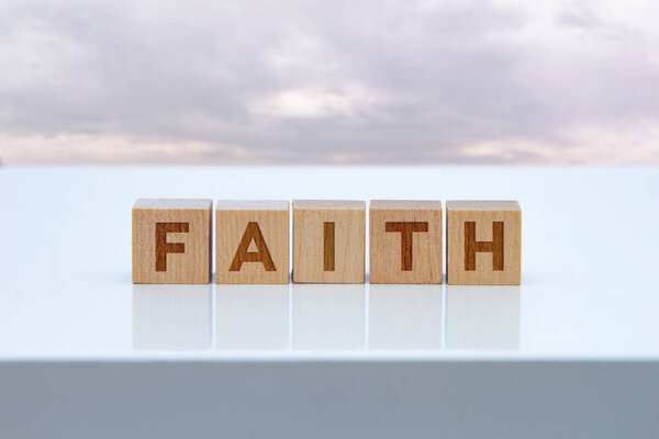 Знак "Вера" на деревянных блоках, сидящих на белом столе.