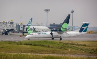 Calgary, Alberta, Kanada. 16 Ekim 2025. İki WestJet uçağı yoğun bir havaalanında, biri turbo pervaneli diğeri de Boeing 737.