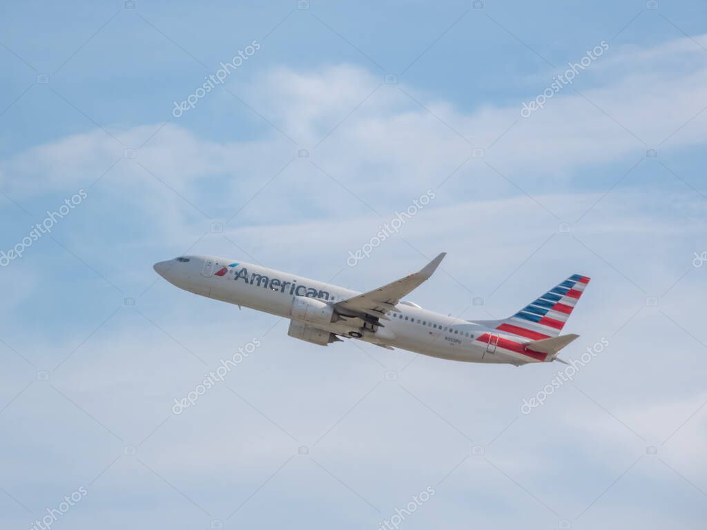 Chicago, Illinois, USA. Oct 15, 2025. An American Airlines plane, with its distinctive red, white, and blue tail, ascends into a bright, cloudy sky.