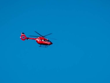 Calgary, Alberta, Kanada. 17 Ekim 2025. Canlı bir kırmızı yıldız helikopteri, açık mavi gökyüzüne doğru zarif bir şekilde süzülür. Uçuşta parlak tasarımını ön plana çıkarır..