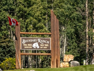 Calgary, Alberta, Kanada. Sep 4, 2025. Sınır Çiftliği için bir ahşap tabela Kanada bayrağının yanında duruyor, ziyaretçileri yemyeşil ortamda gezintilere ve batı tarzı deneyimlere davet ediyor..
