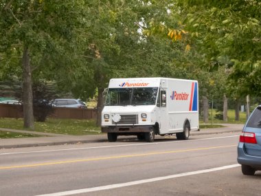 Calgary, Alberta, Kanada. 16 Ekim 2025. Beyaz bir Purolator teslimat kamyonu, parlak bir günde, yemyeşil ağaçlar tarafından çerçevelenmiş, yol kenarına park edilmiştir..