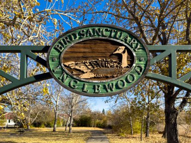 Calgary, Alberta, Kanada. 23 Ekim 2025. Bir davetiye işareti Inglewood Kuş Sığınağı 'nın girişini işaret ediyor. Parlak bir sonbahar gökyüzünün altında, ağaçlar parlak altın yapraklar sergiliyor..