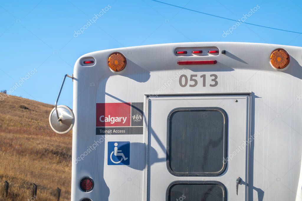 Calgary, Alberta, Canada. Oct 28, 2025. The rear view of a white Calgary Transit Access bus, displaying its logo, vehicle number, and handicap accessibility symbol, under blue sky.