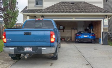 Calgary, Alberta, Kanada. 2 numara, 2025. Mavi Toyota Tundra garaj yolunda mavi bir spor araba bej bir banliyö evinin açık garajında görünür.