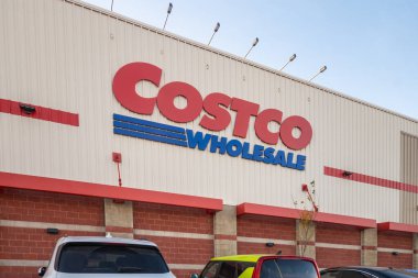 Calgary, Alberta, Kanada. 1 Kasım 2025. Costco toptancı dış görünüşü koyu kırmızı logo, tuğla ve metal cephe, park etmiş araçlar ve mavi gökyüzünün altında ışık direklerini gösteriyor.