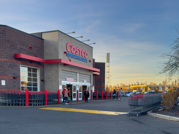 Калгари, Альберта, Канада. 1 ноября 2025 года. Costco Оптовая внешняя показывая знак магазина, выстроенные тележки, клиентов и прилегающей заправке под ясным небом
