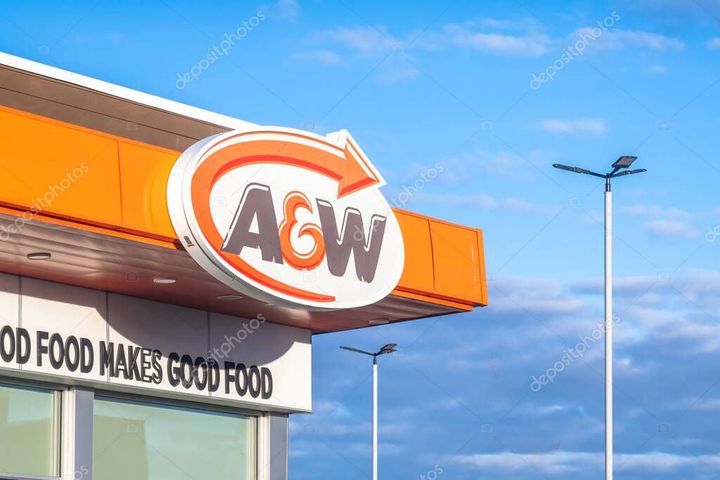 Calgary, Alberta, Canada. Nov 1, 2025. A and W exterior sign on an orange and white building showing the logo and partial slogan under a blue sky with streetlights
