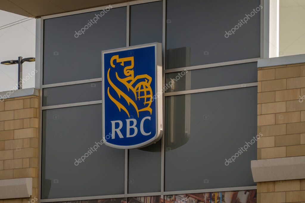 Calgary, Alberta, Canada. Nov 1, 2025. RBC branch exterior showing blue and yellow lion-and-globe logo mounted on glass and beige brick facade identifying the bank location