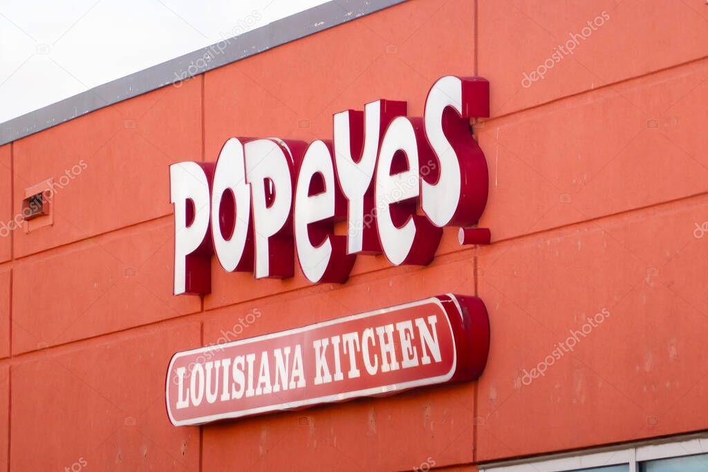 Calgary, Alberta, Canada. Nov 1, 2025. Popeyes Louisiana Kitchen exterior signage on an orange wall showing the brand logo and red 