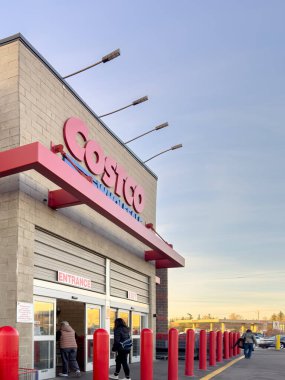 Calgary, Alberta, Kanada. 2 numara, 2025. Costco toptan girişi kırmızı çıkıntılı, kalın ve otomatik sürgülü kapılar müşteriler açık bir gökyüzünün altında girip çıkarken.