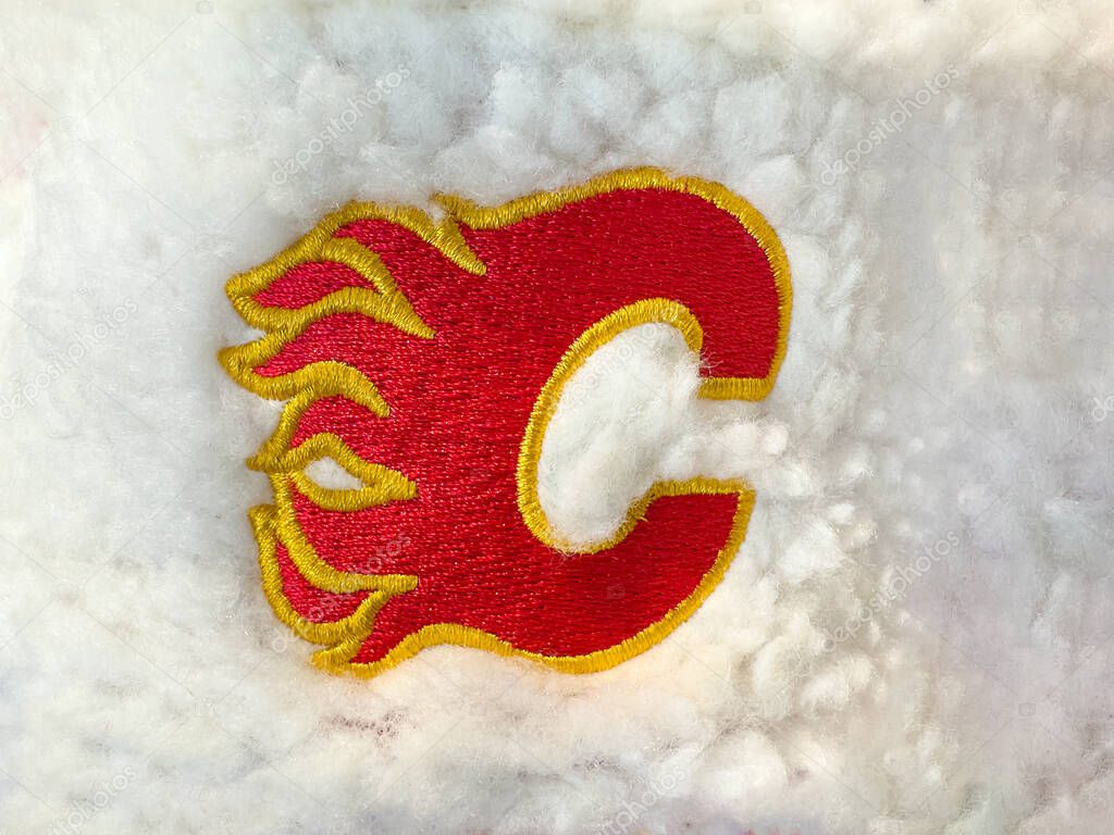 Calgary, Alberta, Canada. Nov 2, 2025. Close-up of an embroidered Calgary Flames red C logo with yellow flames on white fluffy fabric, sports merchandise detail.