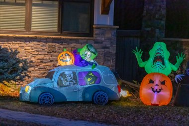 Calgary, Alberta, Kanada. 8 Kasım 2025. Gece vakti ön bahçedeki cadılar bayramı görüntüsü: Bir arabada aydınlatılmış şişme iskeletler Frankenstein, Jacko 'Lantern ve taş bir evin yanındaki yeşil hayalet..