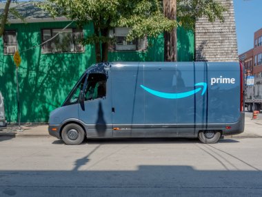 Chicago, Illinois, ABD. 11 numara, 2025. Mavi Amazon Prime minibüsü görünür logosu olan bir caddeye park edilmiş. Yakınındaki ağaçların gölgeleri ve çevresindeki binaların gölgeleri..