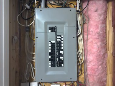 Tamamlanmamış elektrik tesisatı, kablolar, izolasyon ve ahşap çiviler etiketli bir konut sigortası paneline yakın çekim..