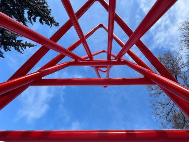 Calgary, Alberta, Kanada. 2 numara, 2025. Olimpik Oval Ofis 'in kuzey girişinde mavi gökyüzünü ve ağaçları çerçeveleyen kırmızı çeliğin alçak açılı görüntüsü, güçlü geometrik çizgiler..