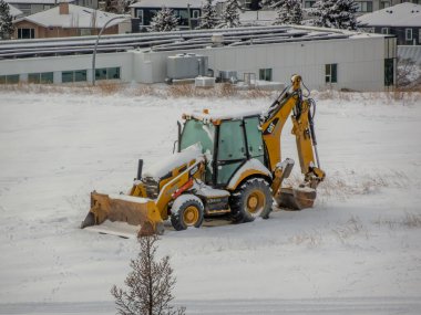 Calgary, Alberta, Kanada. 27 Kasım 2025. Sarı bir Caterpillar 420F serisi kepçe yükleyici bir inşaat alanında çalışıyor, kentsel altyapı geliştirme için toprak taşıyor..